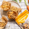 Des muffins sur une assiette reposent à côté d'un paquet de noix Seeberger, décoré de carottes sur une nappe.