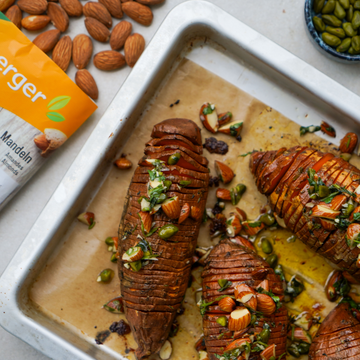 Gebackene Süßkartoffeln, garniert mit gehackten Mandeln und Kräutern, auf einem Blech mit Verpackung.