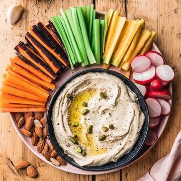 Ein Teller mit Hummus und Gemüse-Sticks auf einem Holztisch arrangiert.