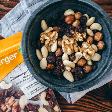 Schüssel mit Nüssen und Rosinen steht auf Tisch neben Studentenfutter-Verpackung.